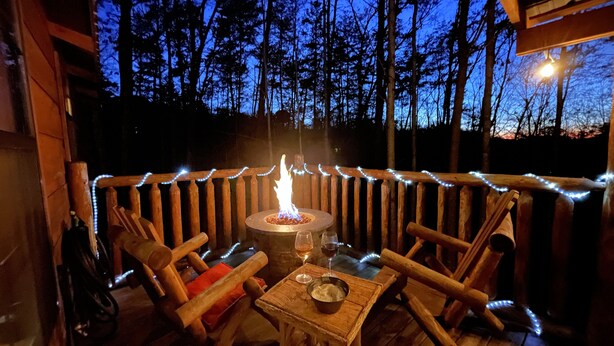 An outdoor seating area with wooden benches and a table, surrounded by a wooden fence with string lights. - Cozy Bear: A Dreamy Cabin Hideout for Two, Gatlinburg & Pigeon Forge - SPECIALS (Pigeon Forge)