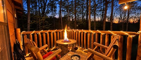 An outdoor wooden deck with a fire pit, seating, and string lights.