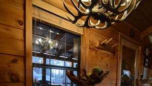 A rustic wooden interior with a large window, a chandelier made of antlers, and a wooden table with a bowl of fruit. - Cozy Bear: A Dreamy Cabin Hideout for Two, Gatlinburg & Pigeon Forge - SPECIALS (Pigeon Forge)