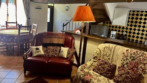 Un salón acogedor con un sofá de cuero, cojines estampados, una mesa de centro de madera y un comedor con mantel estampado.