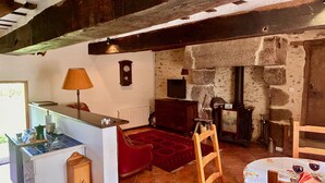 Un interior rústico con pared de piedra, un banco de madera, un tapete rojo, una mesita con vasos y una lámpara.