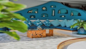 Un vestíbulo moderno con una pared azul decorada con varios objetos ornamentales, un área de descanso con cojines estampados y una mesa de centro de madera.