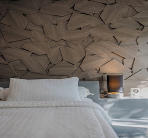 Ein modernes Schlafzimmer mit geometrischem Wanddesign aus Holz, einem Bett mit weißen Leinen und einem Nachttisch mit Lampe.