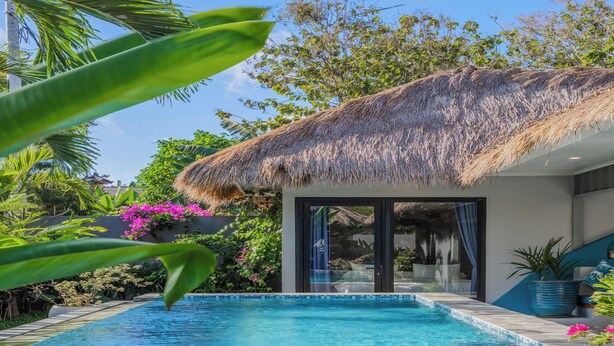 Una piscina con techo de paja, rodeada de abundante follaje y plantas con flores.