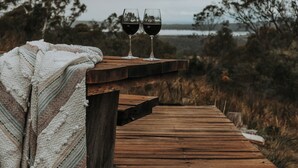 A wooden deck with two glasses of red wine and a white knitted blanket.