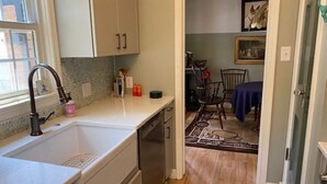 A kitchen with a sink, cabinets, and a dishwasher. There is a dining area with a table and chairs visible through an open door.