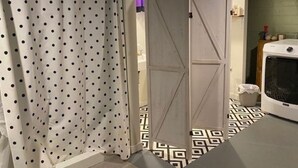 A bathroom with a polka dot shower curtain, a white door, and a patterned floor.