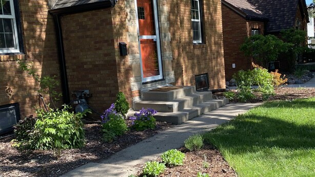 A brick house with a red door, a small front porch, and a well-maintained garden.