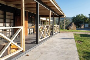 Un espace extérieur abrité, doté de poutres en bois et d’un sol en béton, qui mène à un bâtiment avec de grandes fenêtres et une enseigne sur laquelle on peut lire « SILVER ».