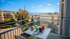 A balcony with a table set for breakfast, overlooking a cityscape and the sea.