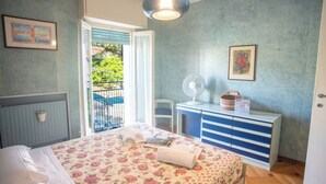 A bedroom with a bed, a dresser, a fan, and a window with a view of greenery.