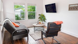 A room with a bed, a chair, a small table, a plant, and a TV on the wall. - Cozy and Gorgeous 2BR 1BA Near Amazing Downtown (San Antonio)
