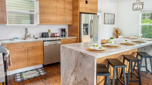 A modern kitchen with wooden cabinets, a stainless steel refrigerator, and a marble island with bar stools. - Cozy and Gorgeous 2BR 1BA Near Amazing Downtown (San Antonio)