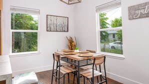 A dining area with a wooden table, chairs, and a view of trees through the windows. - Cozy and Gorgeous 2BR 1BA Near Amazing Downtown (San Antonio)
