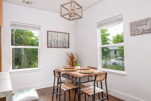 A dining area with a wooden table, chairs, and a view of trees through the windows. - Cozy and Gorgeous 2BR 1BA Near Amazing Downtown (San Antonio)