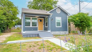 A single-story house with a front porch, a small attached garage, and a well-maintained lawn. - Cozy and Gorgeous 2BR 1BA Near Amazing Downtown (San Antonio)