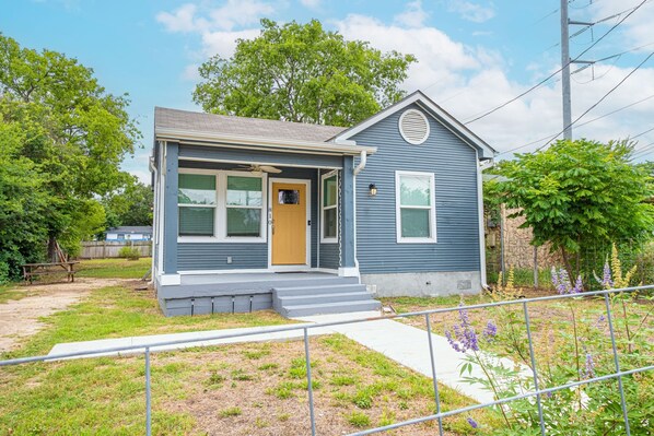 A single-story house with a front porch, a small attached garage, and a well-maintained lawn. - Cozy and Gorgeous 2BR 1BA Near Amazing Downtown (San Antonio)