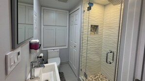 Een moderne badkamer met een douche met glazen wand, een wit wastafelmeubel en een toilet.