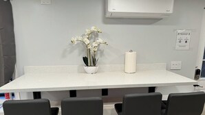 Een keuken met een wit aanrecht, vier zwarte barkrukken, een witte vaas met bloemen en een witte papieren handdoekhouder.