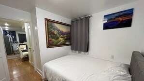 A bedroom with a bed, a gray sofa, a painting, and a window with curtains. - Remodeled 1BR near SF/SFO — parking + EV (South San Francisco)