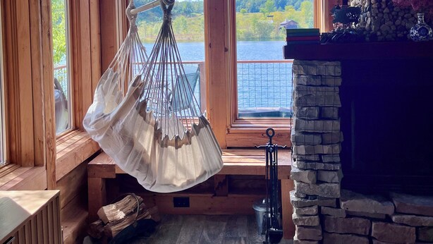 A cozy cabin interior with large windows, a hanging chair, a fireplace, and a view of a lake. - Lakeside Cabin on Private Lake! Perfect for families and couples getaway. (Cascade)