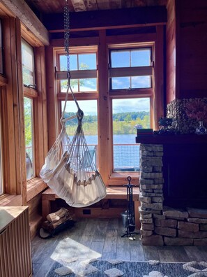 A cozy cabin interior with large windows, a hanging chair, a fireplace, and a view of a lake. - Lakeside Cabin on Private Lake! Perfect for families and couples getaway. (Cascade)