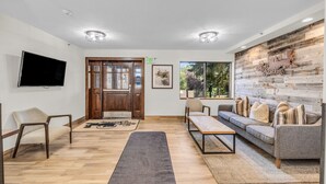 A modern lobby with a wooden floor, a sofa, a TV, and a wall with a rustic design. - Central Park City | Pool + Patio Access (Park City)