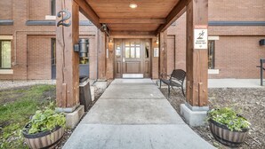 A building entrance with a covered walkway, wooden pillars, and potted plants. - Central Park City | Pool + Patio Access (Park City)