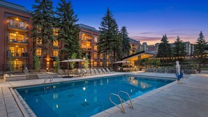 A swimming pool with lounge chairs and umbrellas, surrounded by tall trees and a building with balconies. - Central Park City | Pool + Patio Access (Park City)