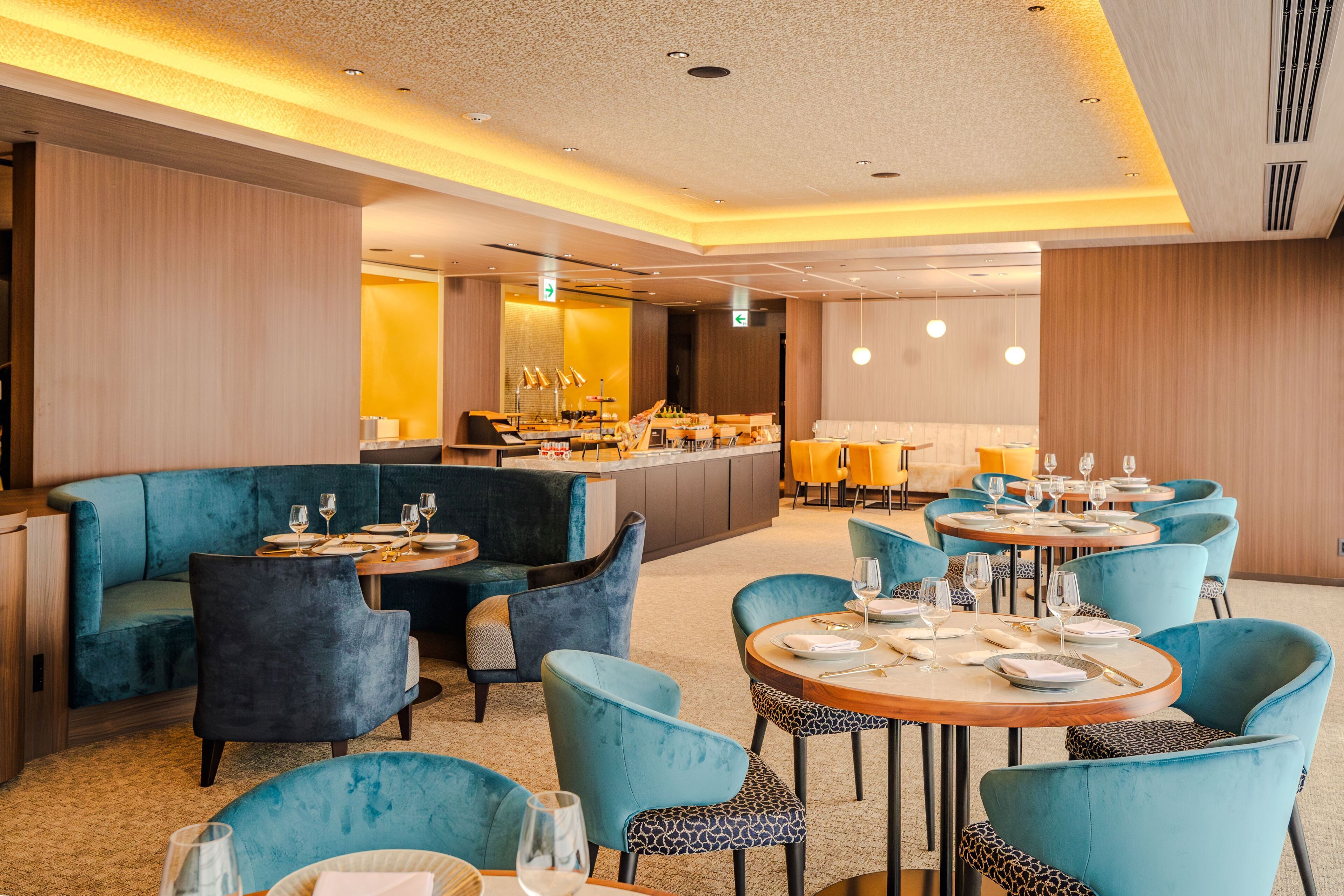 A modern dining area with blue upholstered seating and round tables, featuring a central bar and ambient lighting.