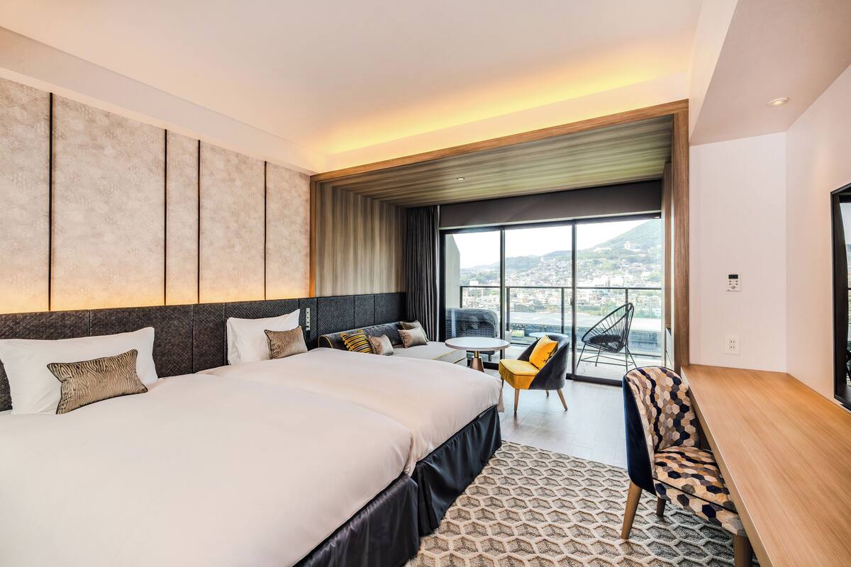 Ett modernt hotellrum med en stor säng, ett litet bord, en stol och en balkong med utsikt över staden.