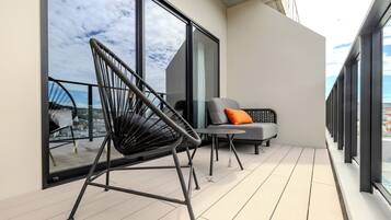A balcony with a black chair, a grey sofa with an orange pillow, and a small table.