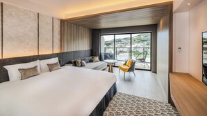 Habitación de hotel moderna con una cama grande, un sofá, una mesita y una silla. La habitación tiene un ventanal con vistas a la ciudad.