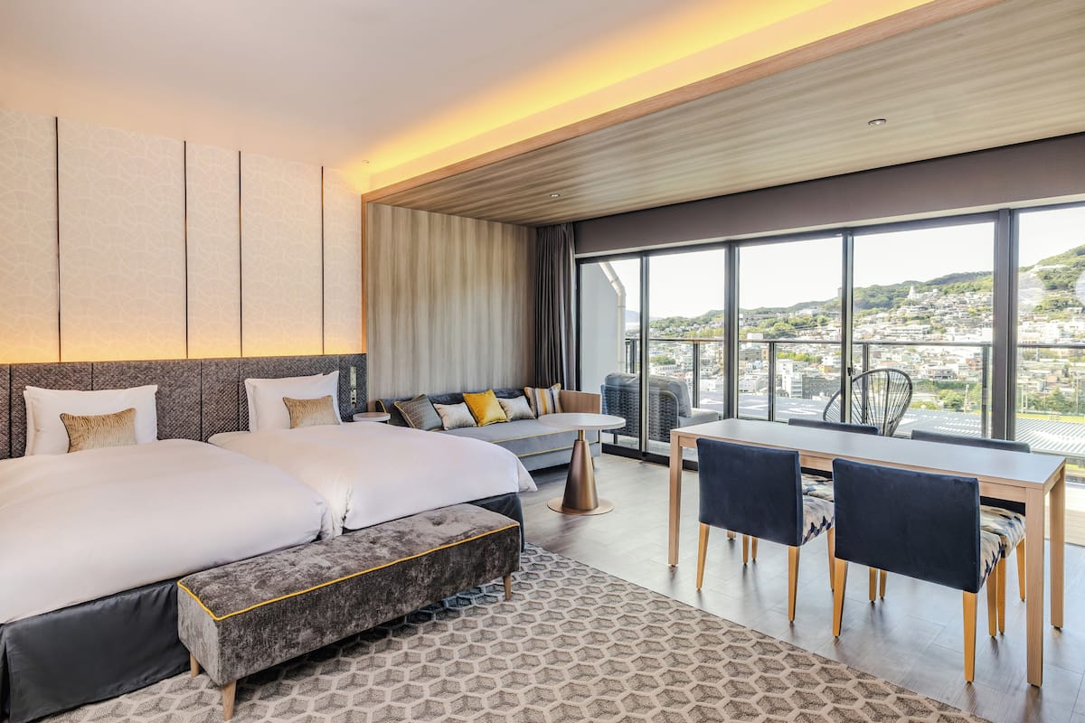 Ett modernt hotellrum med en stor säng, en soffa, ett matbord med stolar och utsikt över staden.