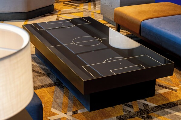 A modern room with a unique, illuminated table resembling a soccer field, a blue sofa, and a patterned carpet.