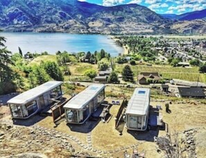 A scenic view of a lake with mountains in the background and a small settlement with several mobile homes. - Modern Glass Pod on Vineyard (Penticton)