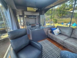 A compact living space with a sofa, a chair, a small kitchen area, and a large window offering a view of the outdoors. - Modern Glass Pod on Vineyard (Penticton)