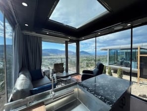 A modern room with a large skylight, a seating area with a sofa and chairs, and a view of the landscape. - Modern Glass Pod on Vineyard (Penticton)