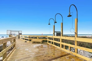 Une terrasse en bois avec une rambarde en bois, un banc et une vue sur la plage et l’océan.