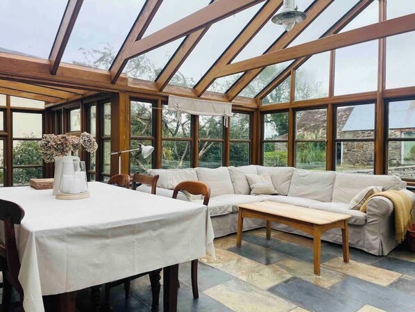 A conservatory with a wooden ceiling, a sofa, a table, and chairs.