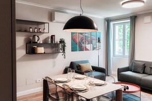 A modern living room with a dining table set for four, a sofa, a coffee table, and a large window.