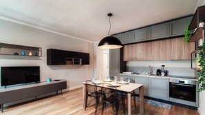 A modern kitchen with grey cabinets, a dining area with a table set for four, and a TV mounted on a wall. - Marinetti Suite 7 - MyHomeinComo (Como)