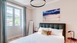 A bedroom with a bed, a painting of a beach scene, a window with curtains, and a bedside table with a lamp. - Marinetti Suite 7 - MyHomeinComo (Como)
