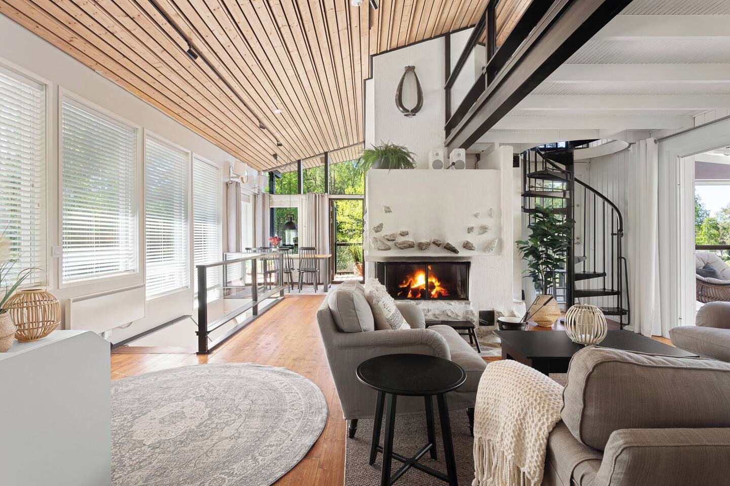 A modern living room with a fireplace, wooden ceiling, and a dining area with natural light.