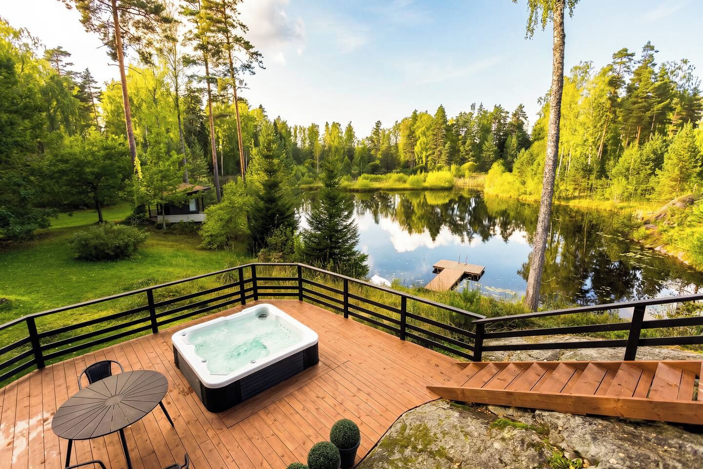 Un bain à remous sur une terrasse en bois, avec vue sur un lac et une forêt.
