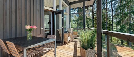 A wooden deck with a table and chairs, a basket of plants, and a glass door leading to an outdoor area.