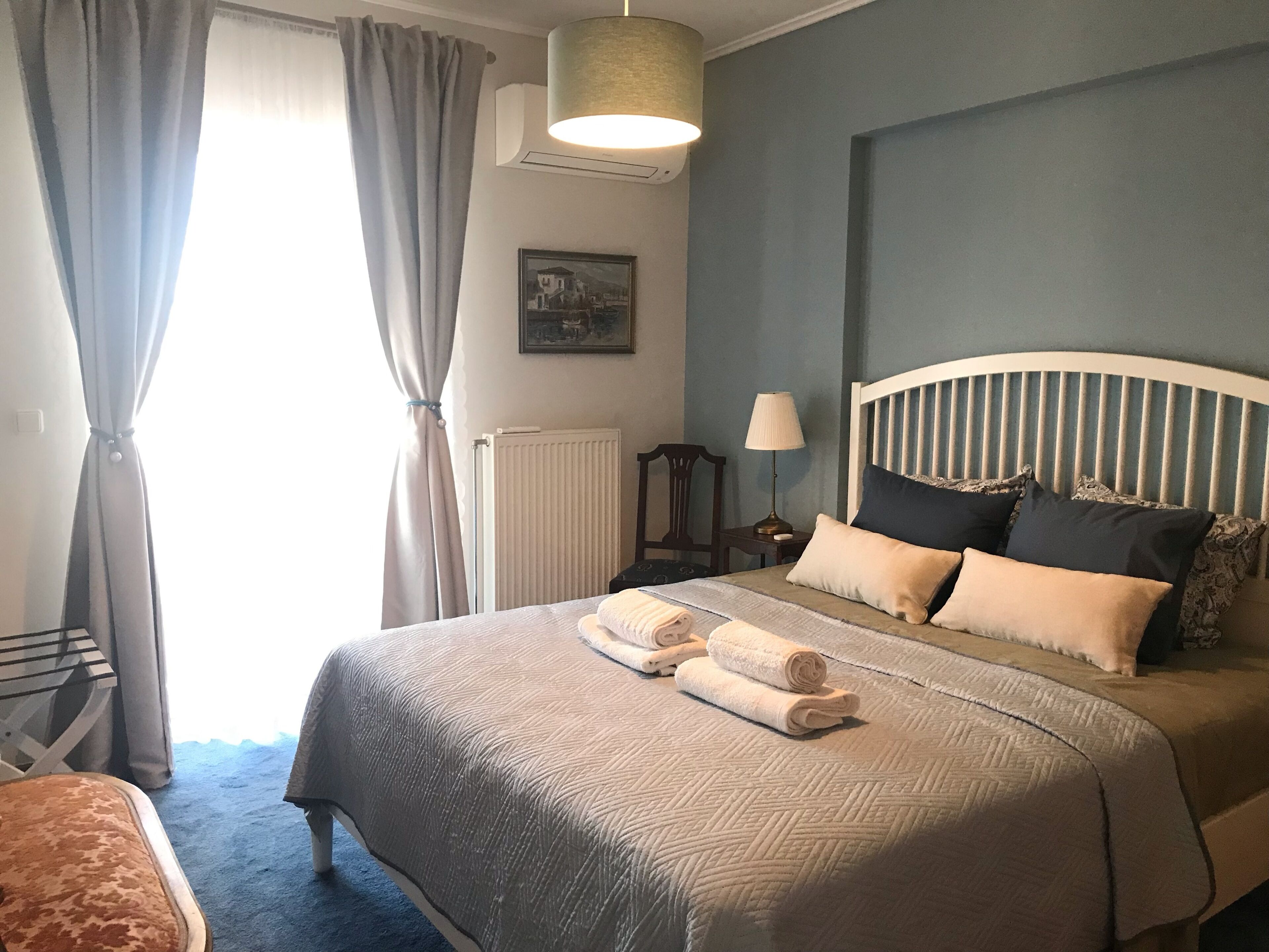A bedroom with a bed, a nightstand, a lamp, a radiator, and a window with curtains.