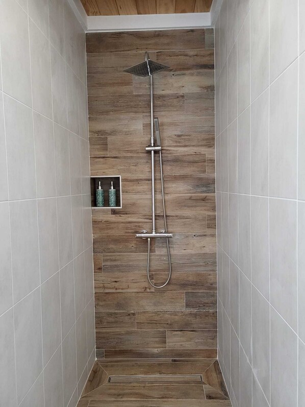 A shower area with a wooden panel wall, a handheld showerhead, and a wall-mounted faucet.