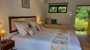 A bedroom with a bed, bedside lamp, and a window with a view of greenery. - FARE MANTA (Moorea-Maiao)