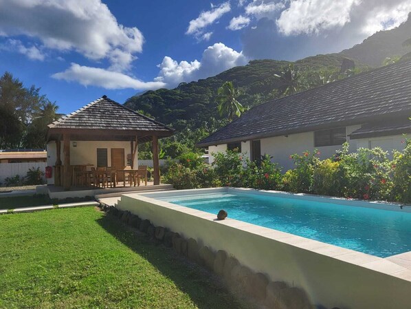 A pool area with a gazebo, a lounge chair, and a building with a tiled roof. - FARE MANTA (Moorea-Maiao)